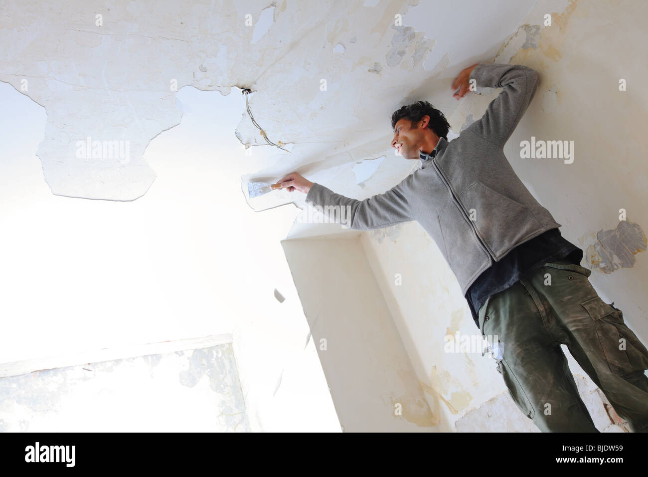 Man Working In Kitchen And Removing Old Paint Of Ceiling