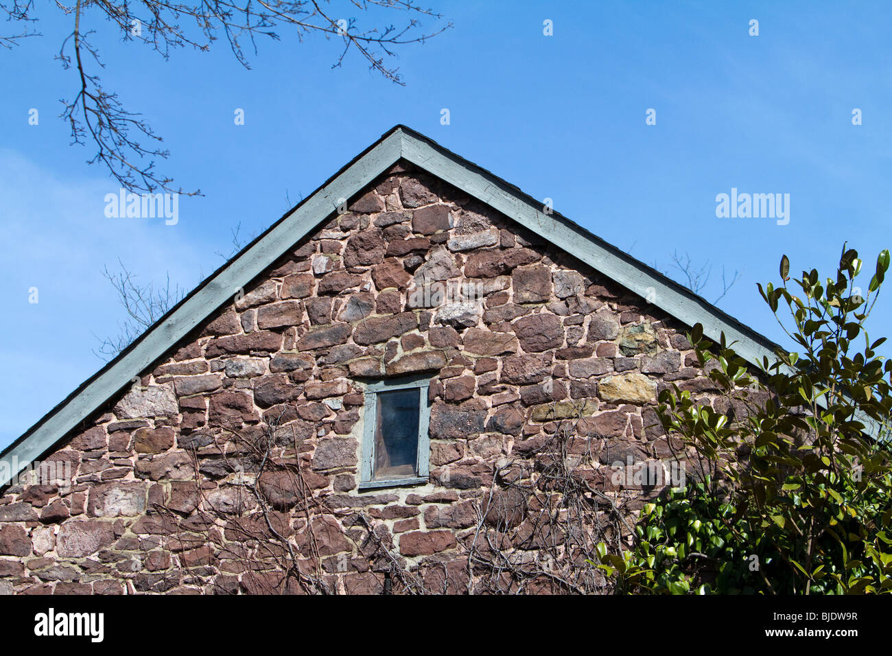 The gable end of a colonial vintage stone barn. Shot against a very blue sky. Stock Photo