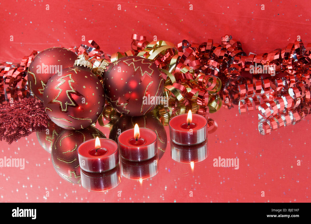 three Christmas baubles with red tealight candles and curly ribbon with reflections Stock Photo