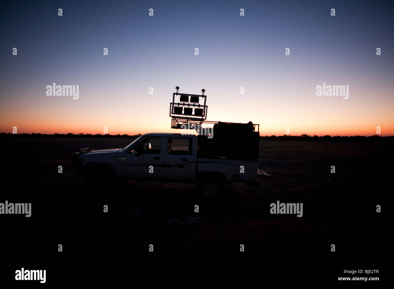 IR lighting rig wagon silhouetted by the setting sun prior to a night film shoot in Africa Stock Photo
