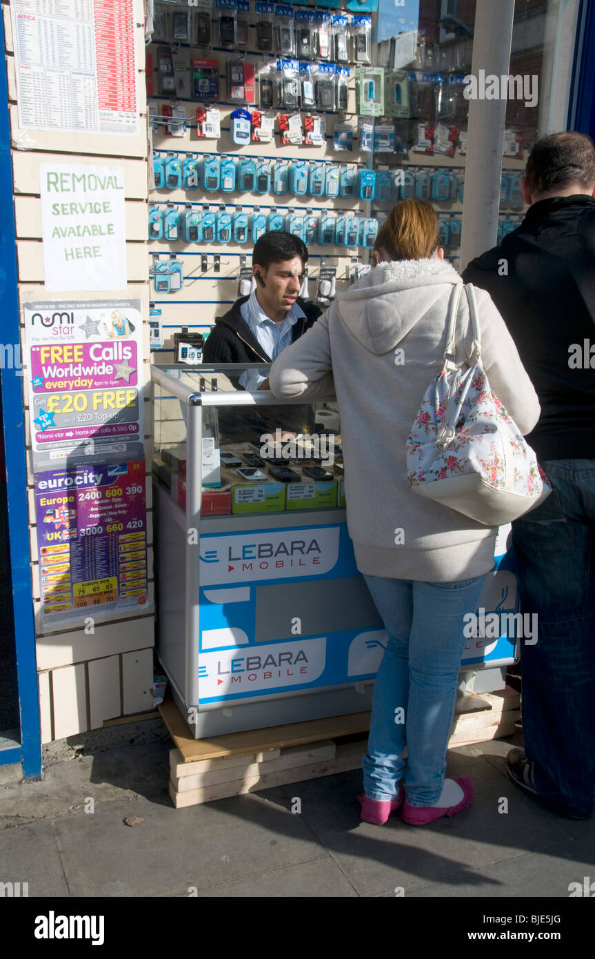 UK. Customers at mobile phone stall next to African and Caribbean DVD