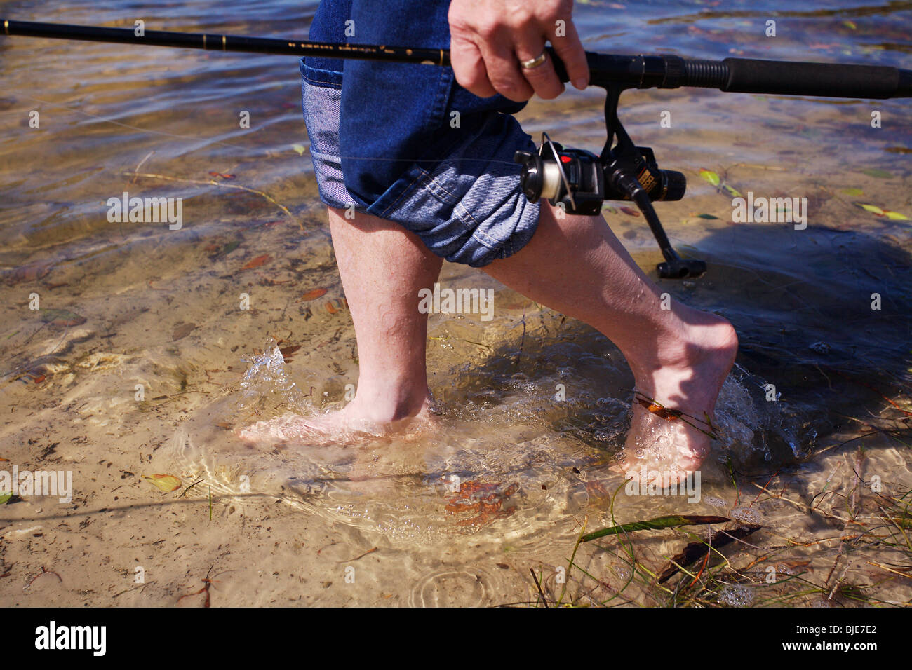 FISHERMAN STANDING IN SHALLOW WATER HOLDING FISHING ROD AND REEL BLUE