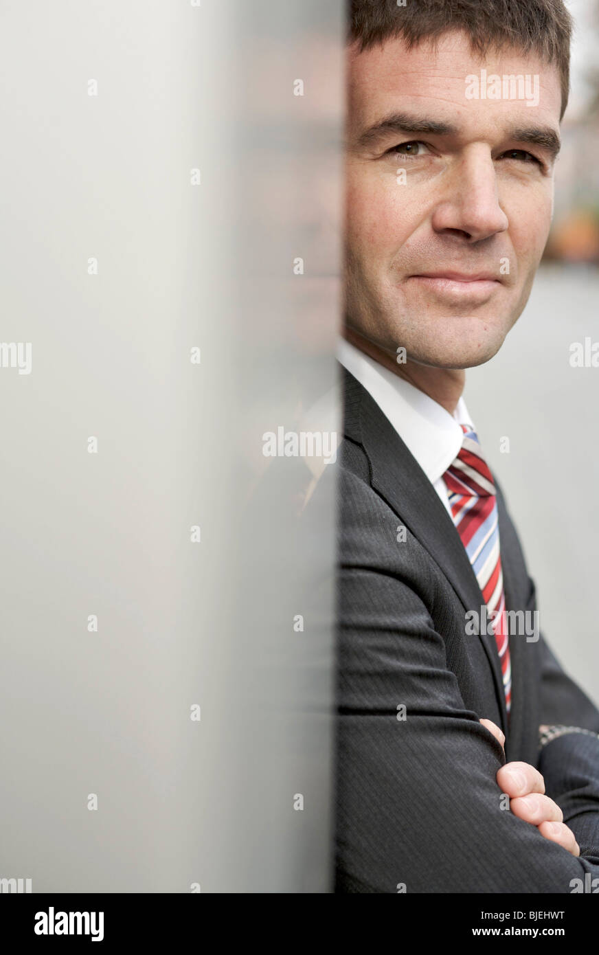 Businessman leaning against wall, eye contact Stock Photo Alamy