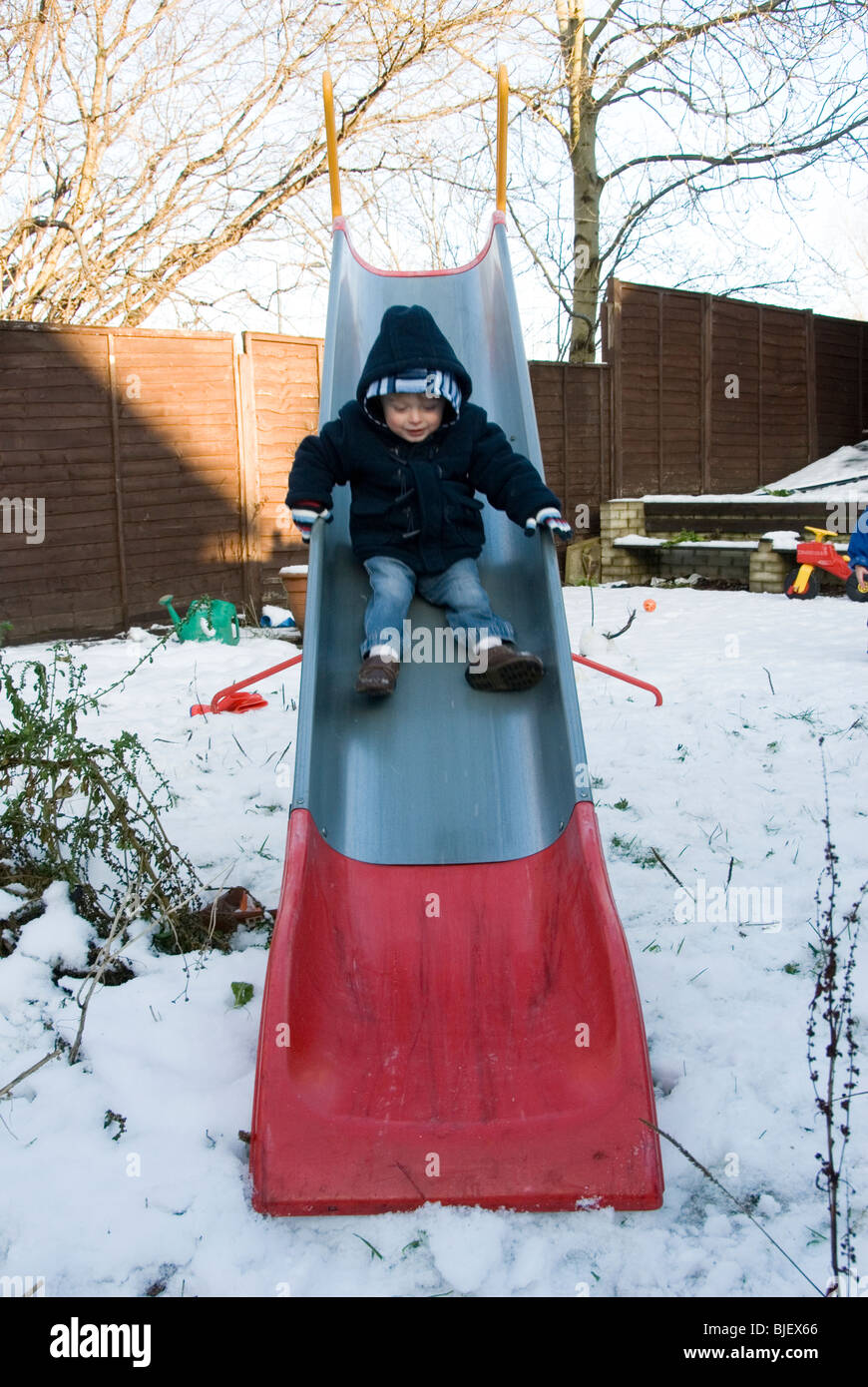 Little Boy Toddler Playing on a Slide in Back Garden in Snow, Christmas Day, Sheffield 2009 Stock Photo