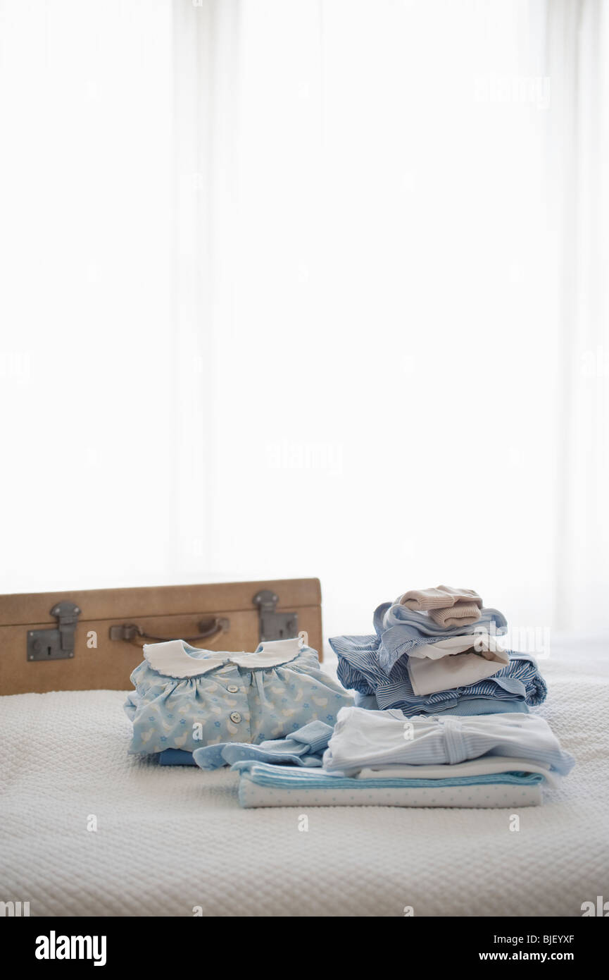 Childrens clothes folded on bed next to suitcase Stock Photo Alamy