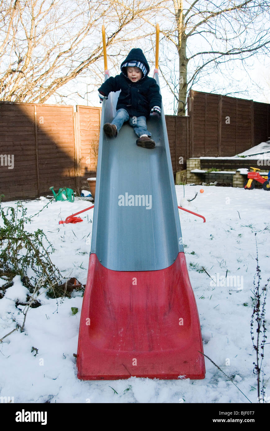 Little Boy Toddler Playing on a Slide in Back Garden in Snow, Christmas Day, Sheffield 2009 Stock Photo