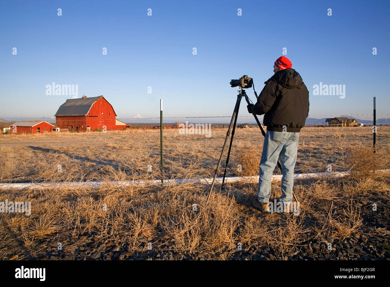 A photographer shoots an old red barn with Mount Jefferson in the background, in central Oregon Stock Photo