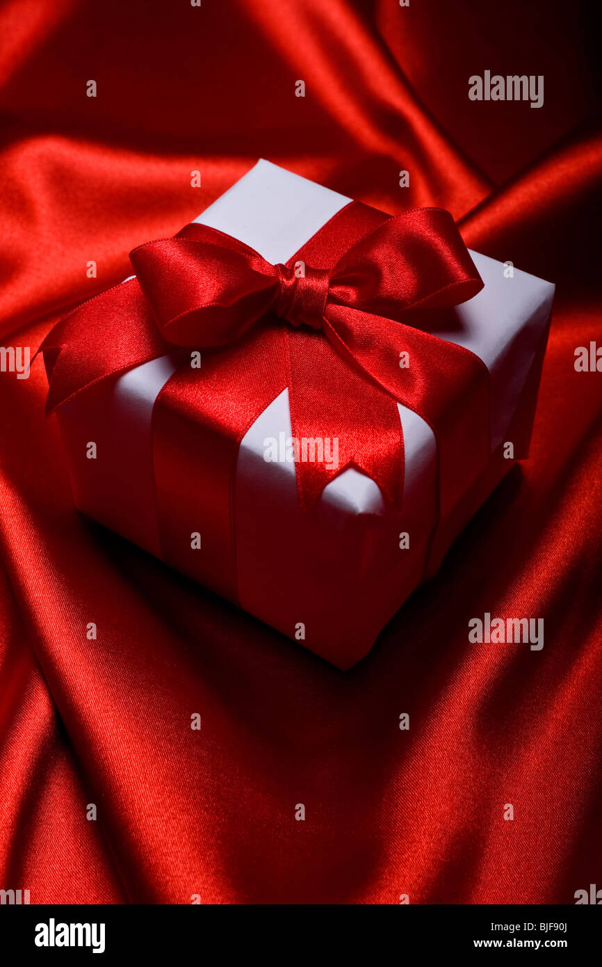 gift with decorative red ribbon on red silk background Stock Photo
