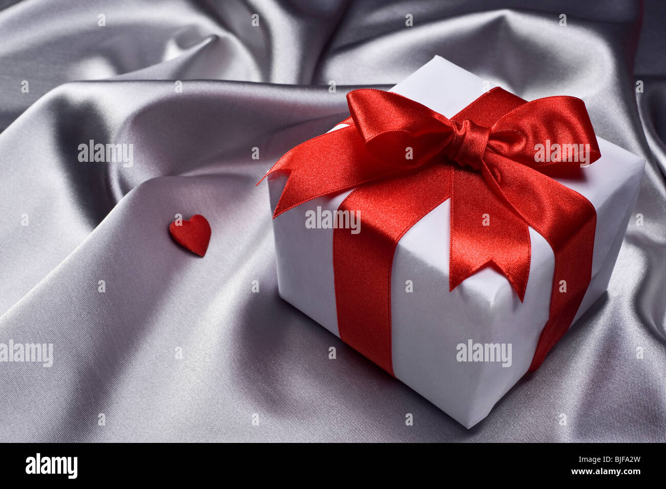 gift with decorative red ribbon on silver silk background Stock Photo