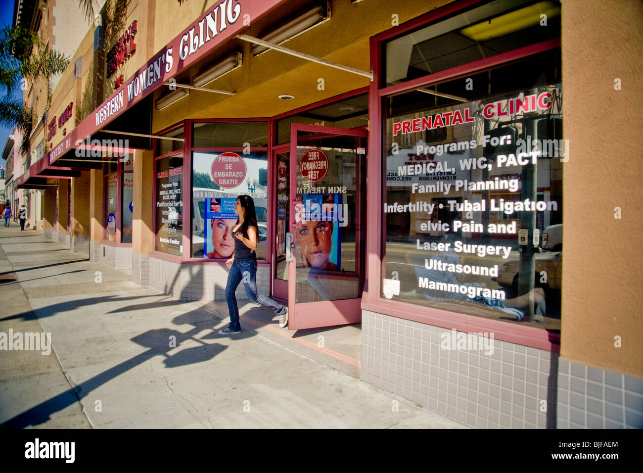 A storefront womens' health clinic lists services in both English and Spanish or 'Spanglish' on window signs in a 'barrio' in CA Stock Photo