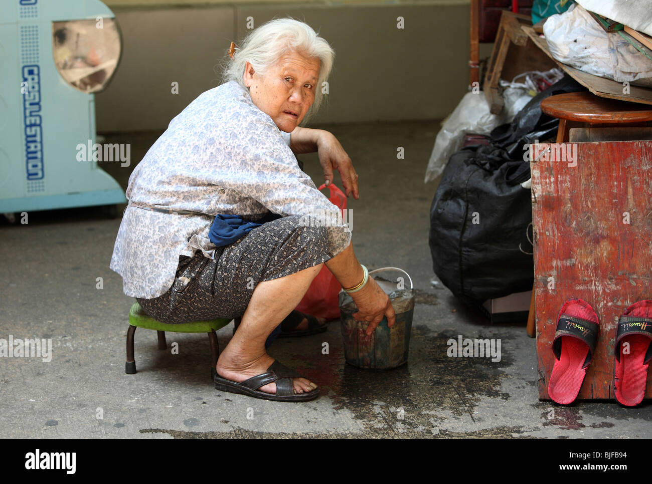 Elderly woman sitting with a bucket of water, Macao, China Stock Photo