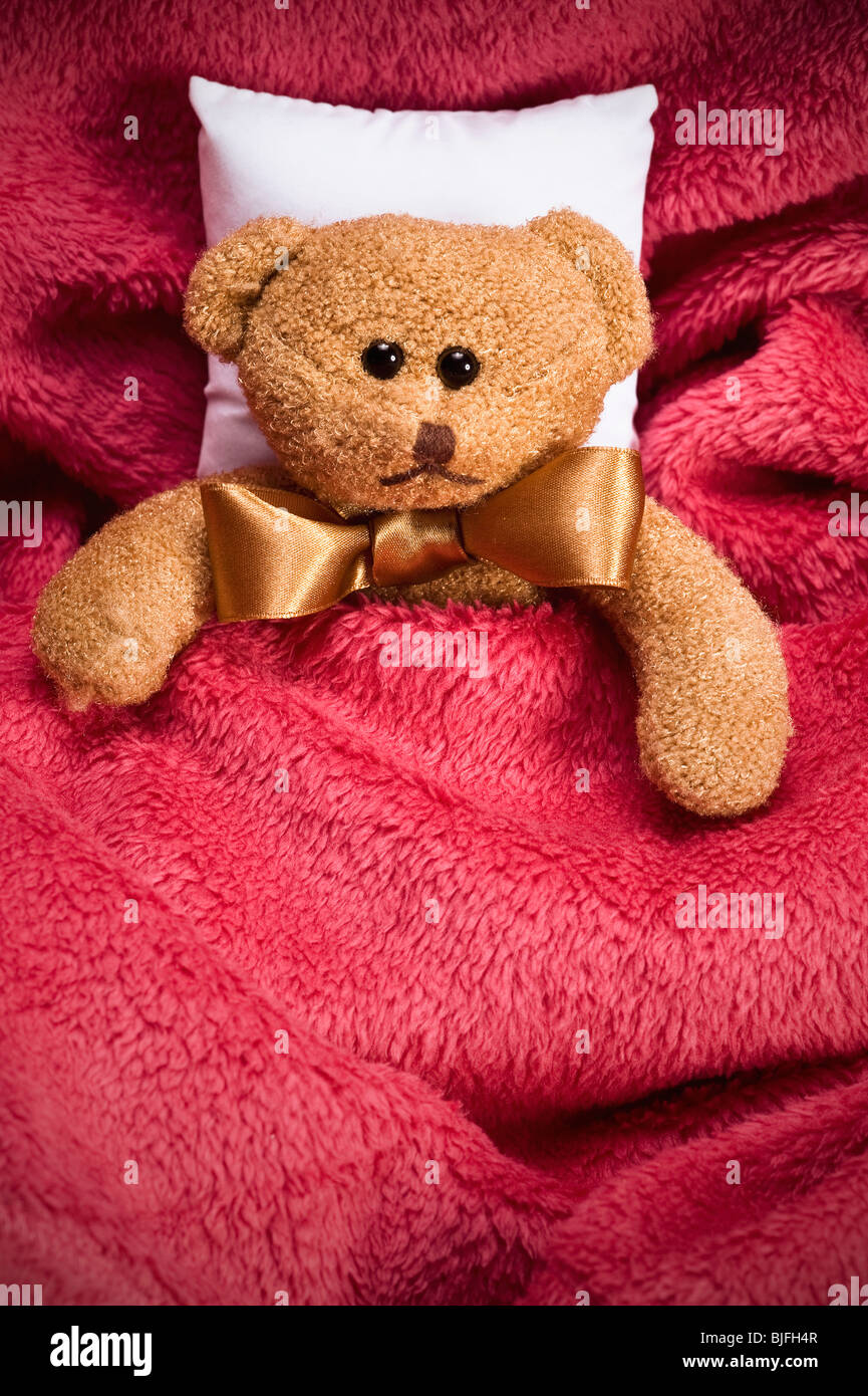 plush teddy bear with bow lying under cosy blanket Stock Photo