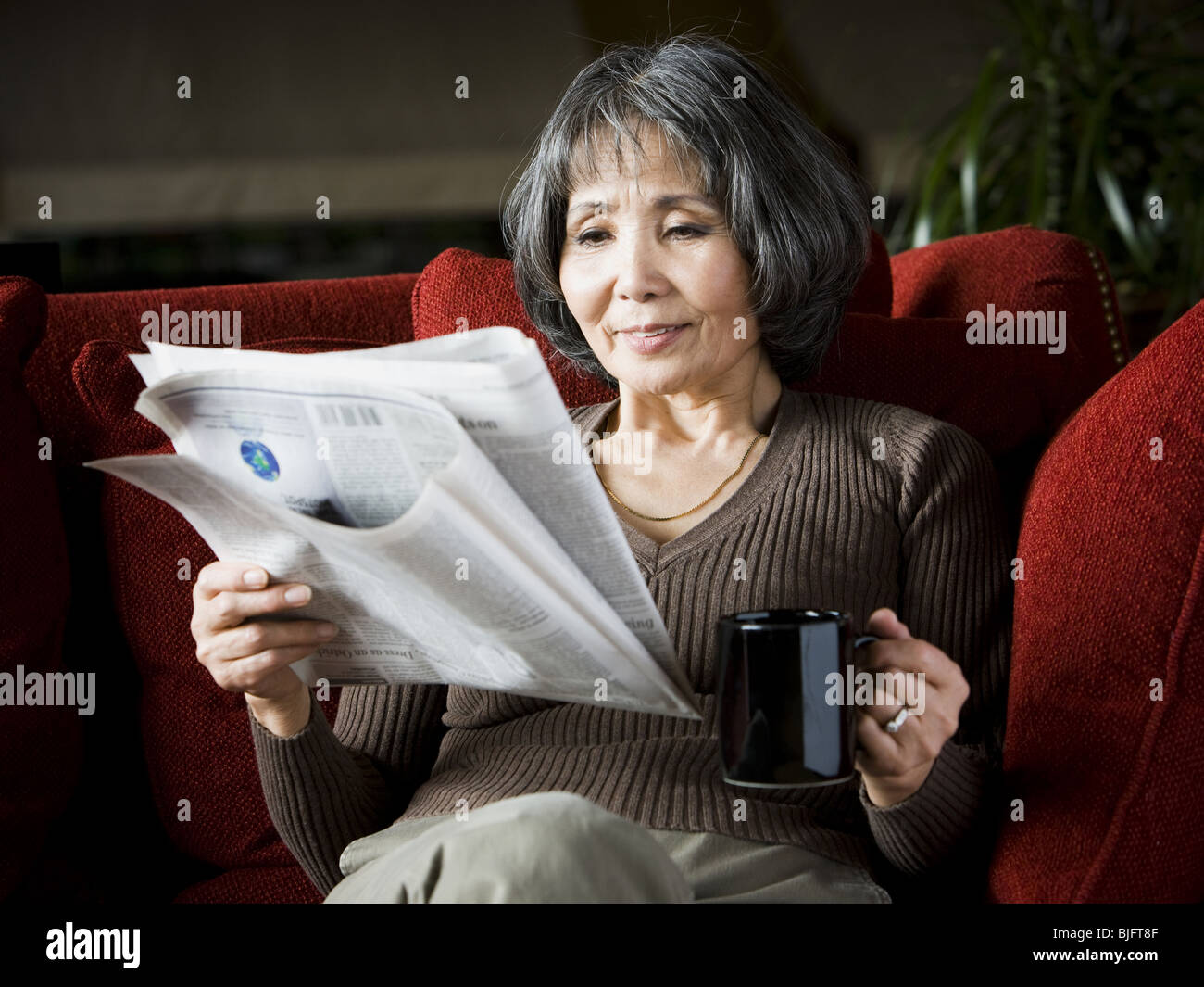 senior woman reading a newspaper on the couch Stock Photo
