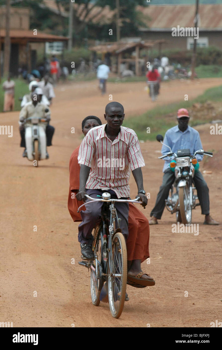 Modes of transport on Africa's dusty roads. A gentlemen gives his friend a lift through the town on his bicycle. Uganda Stock Photo