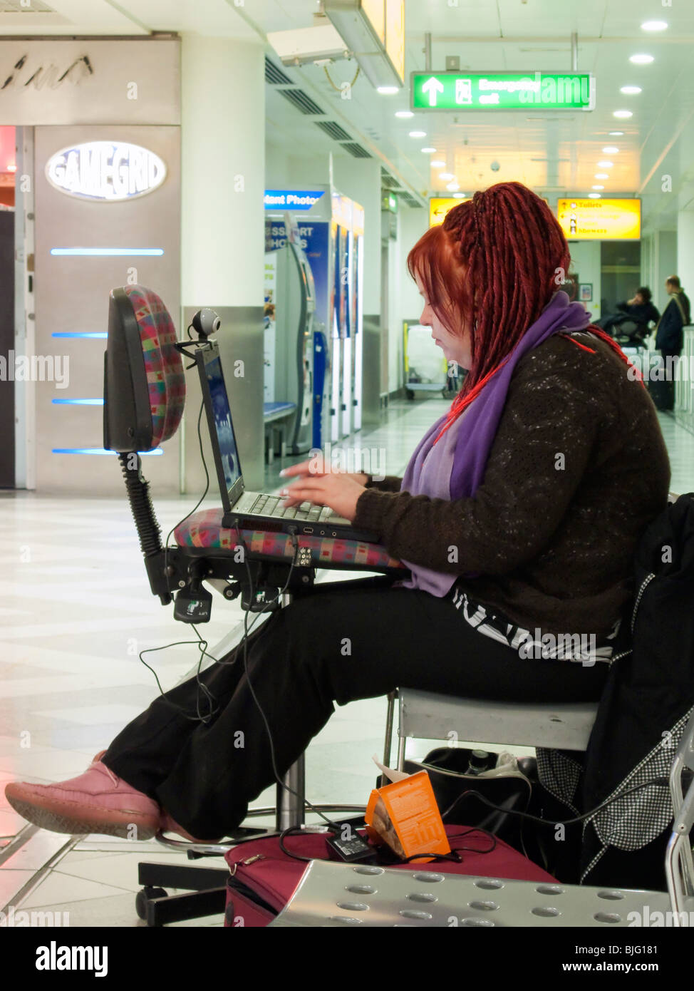 A female airline passenger using a laptop computer in an airport transit area with waiting passengers in the background. Stock Photo
