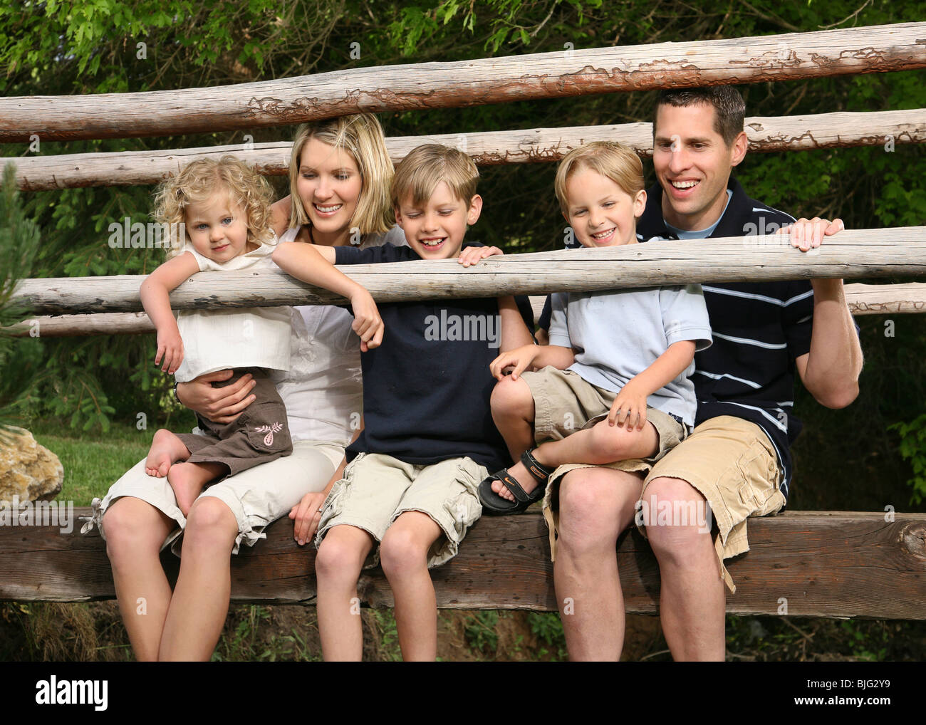 happy young family sitting together on a wood bridge with legs dangling ...