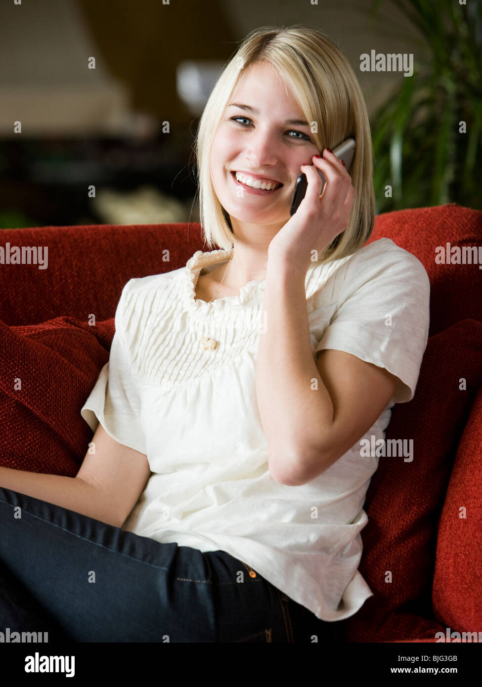 woman using her cell phone on a red sofa Stock Photo