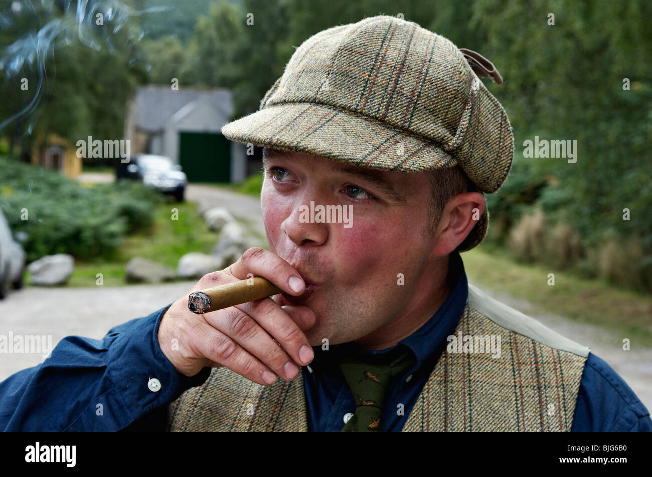 Man in Tweeds and Deerstalker Hat Smoking a Cigar in the Highlands of Scotland Stock Photo