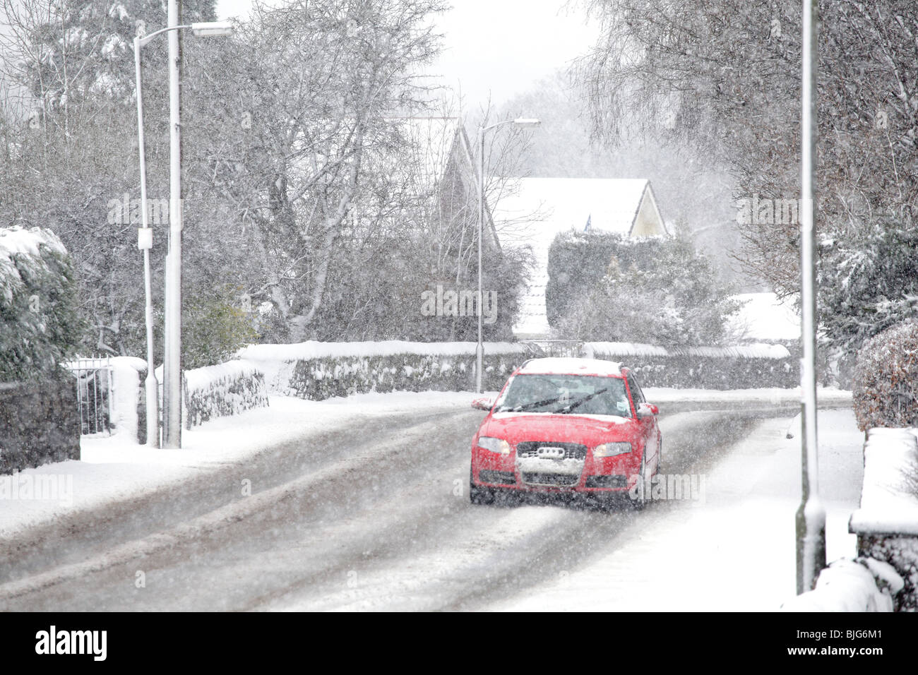 A red car driving in falling snow on Johnshill the main road through