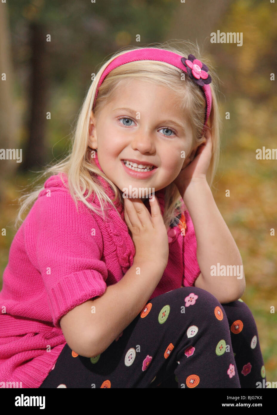 pretty little blond girl in pink sweater sitting outside Stock Photo