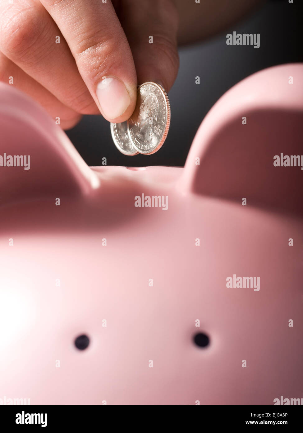 hand putting two quarters in a piggy bank Stock Photo