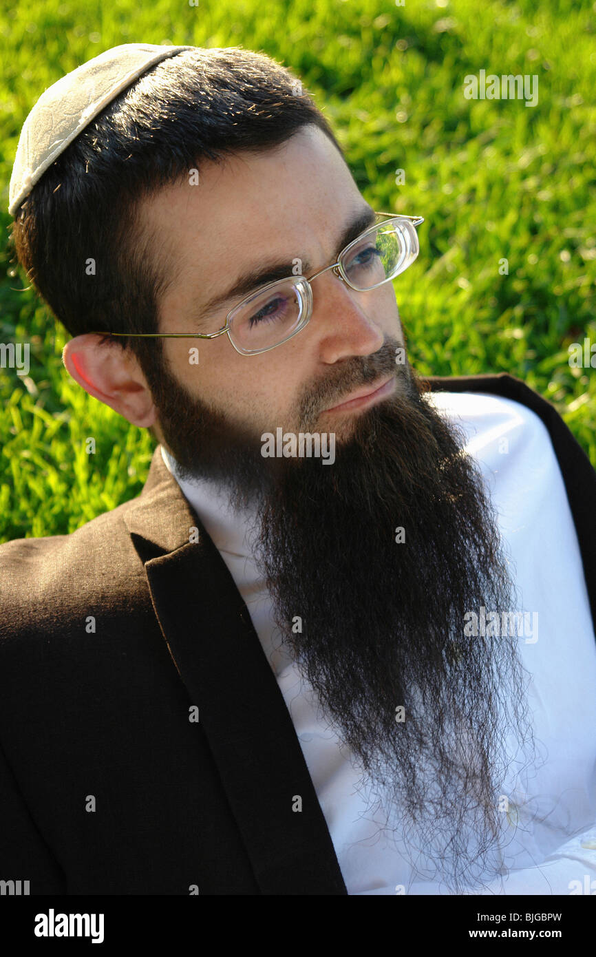 Environmental Portrait of Bearded Hasidic Jewish Man on a Grassy Lawn on a Sunny Day. He is Wearing a Yarmulke and Eyeglasses Stock Photo