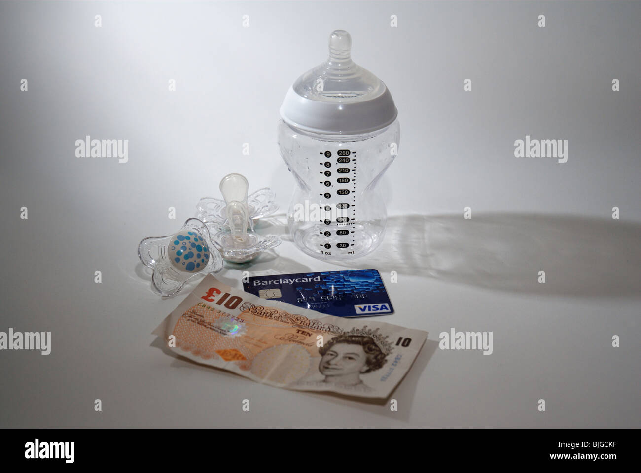 Baby bottle with credit card and UK money to illustrate the cost of having a child and children Stock Photo