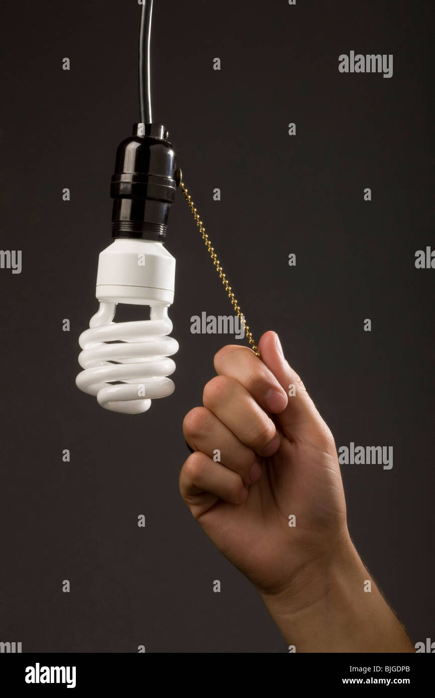 hand pulling chain on energy saving light bulb Stock Photo