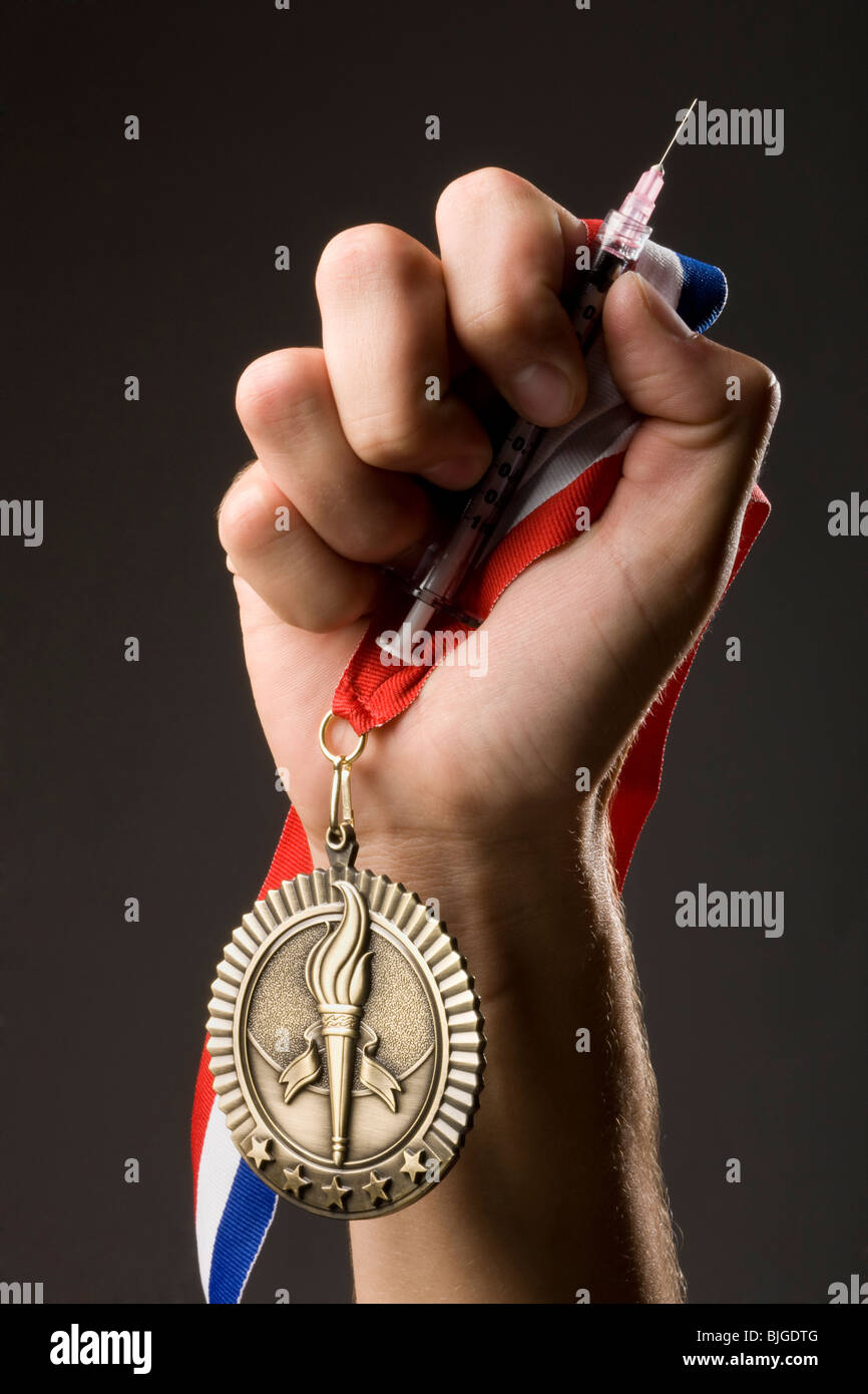 hand holding a gold medal and a syringe Stock Photo