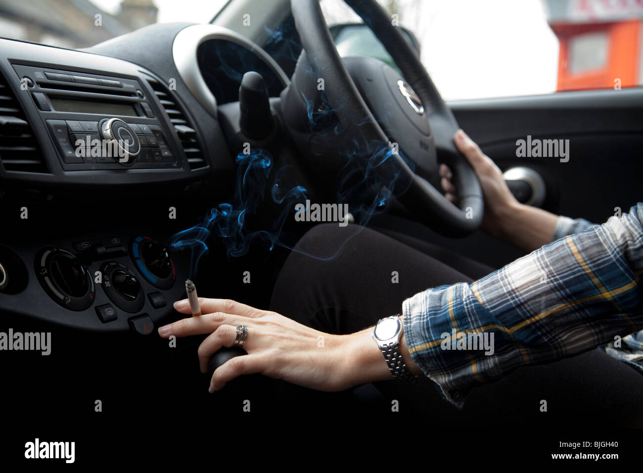 Woman smoking cigarette in car. Doctors in UK are calling for a ban of smoking in cars. Stock Photo