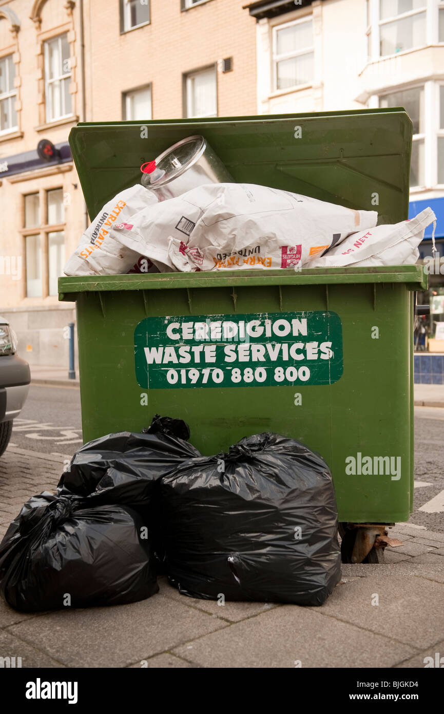 A green wheelie bin overflowing with commercial waste, Aberystwyth Ceredigion WALES UK Stock Photo