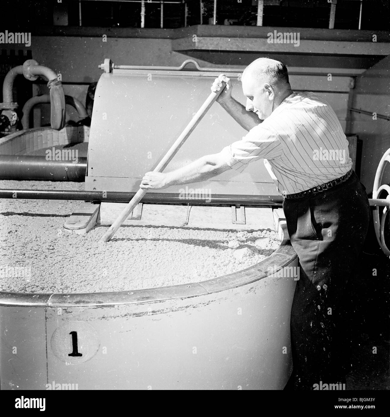 Paper making in the 1950s. Male worker at stirs by hand the pulp