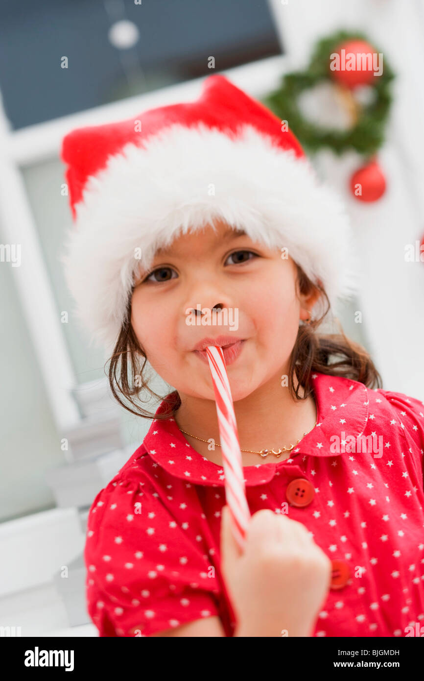 Small girl in Father Christmas hat eating candy cane Stock Photo Alamy