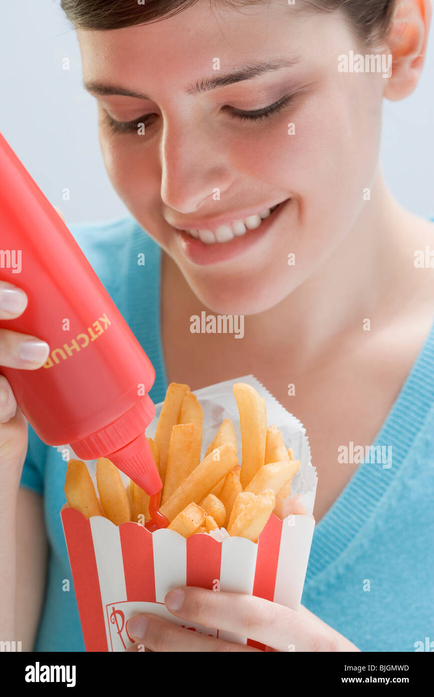 Young woman squeezing ketchup out of bottle onto chips Stock Photo Alamy