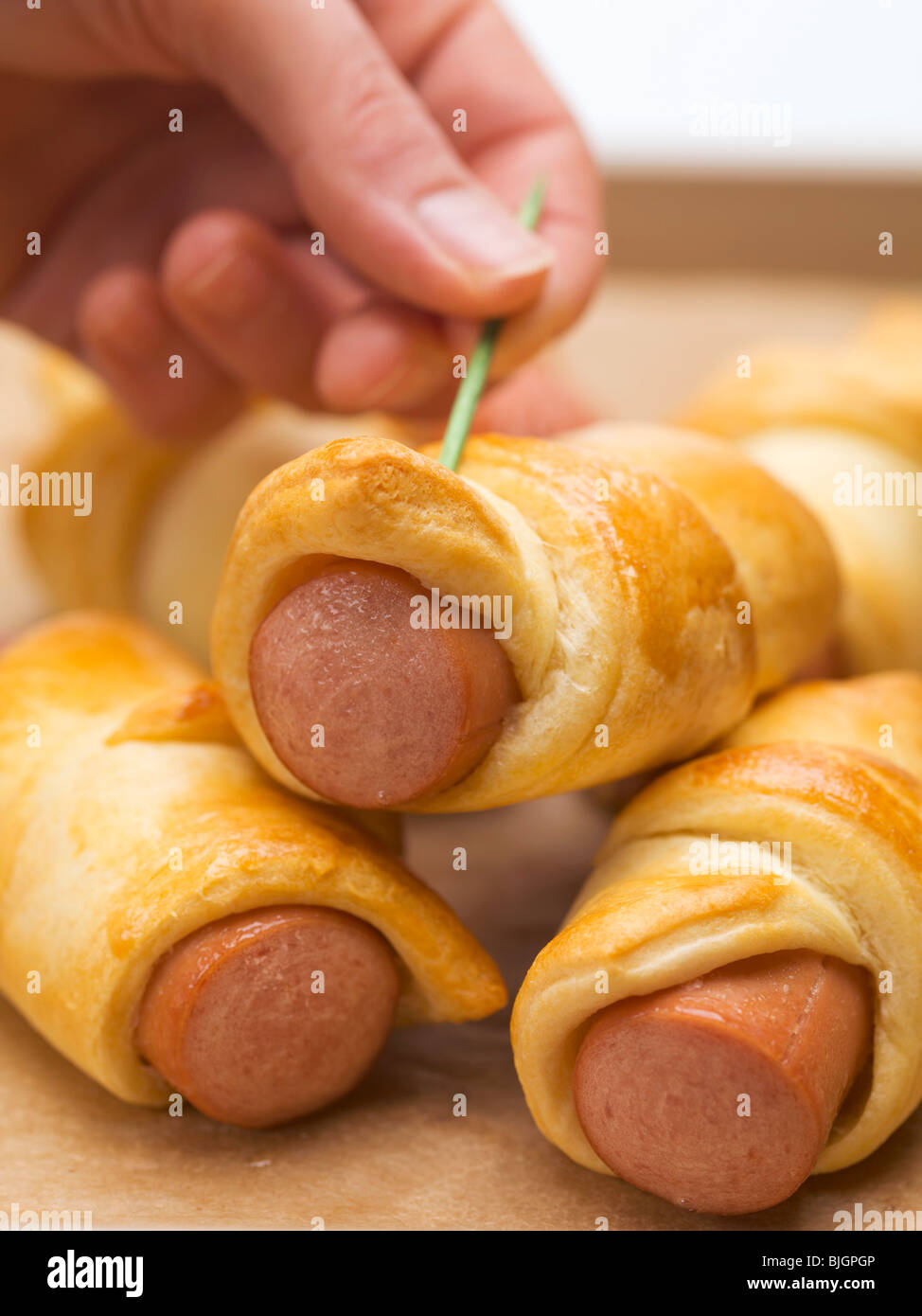 Hand pushing cocktail stick into sausage roll - Stock Photo