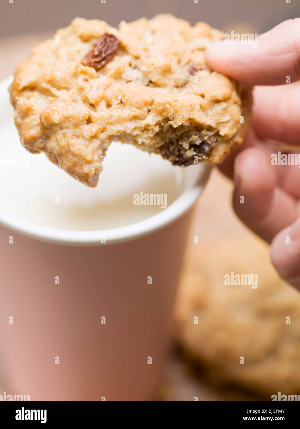 Hand holding cookie over a beaker of milk - Stock Photo