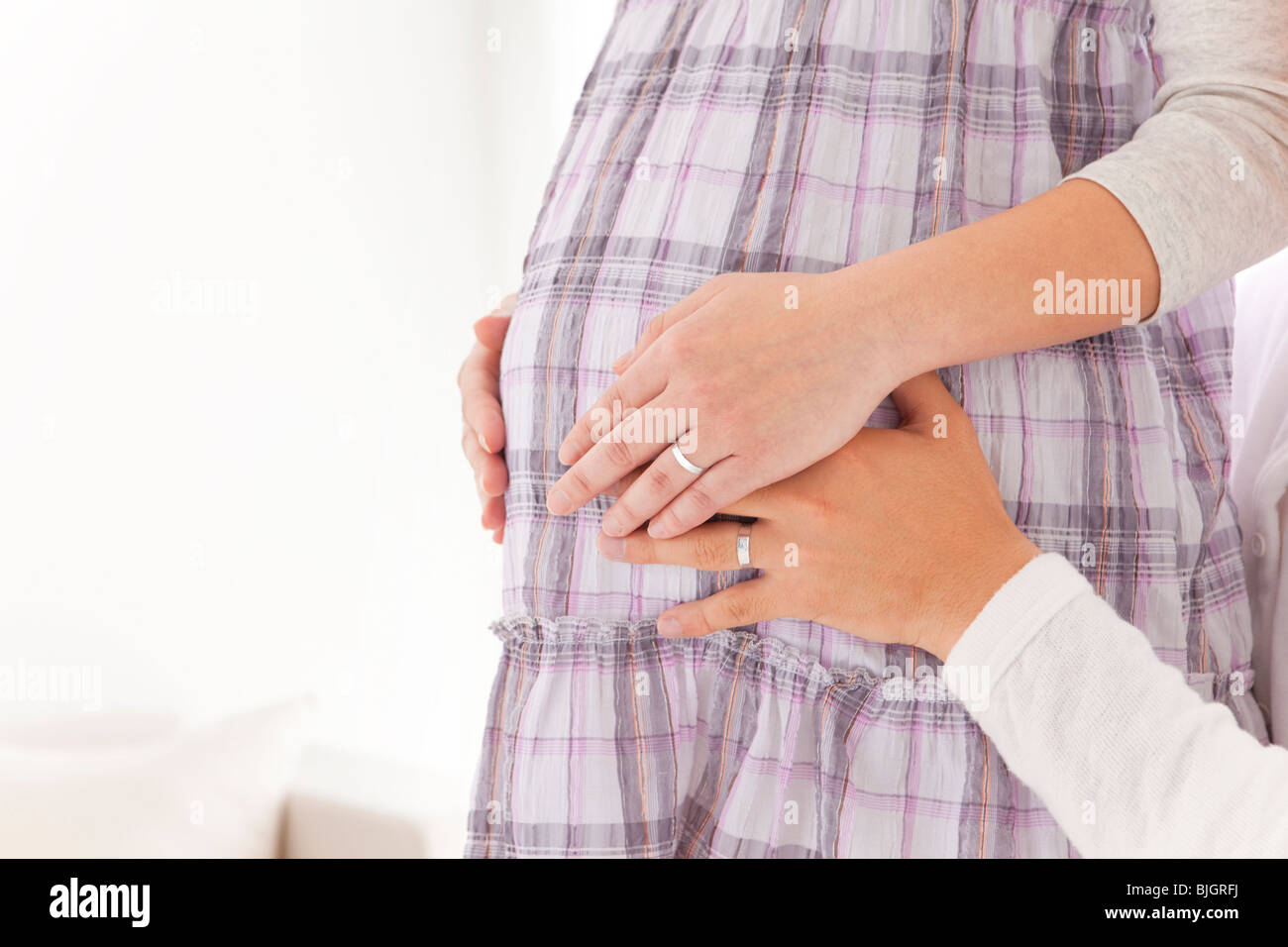 Cropped image of a woman's pregnant midsection with husband's hand touching belly Stock Photo