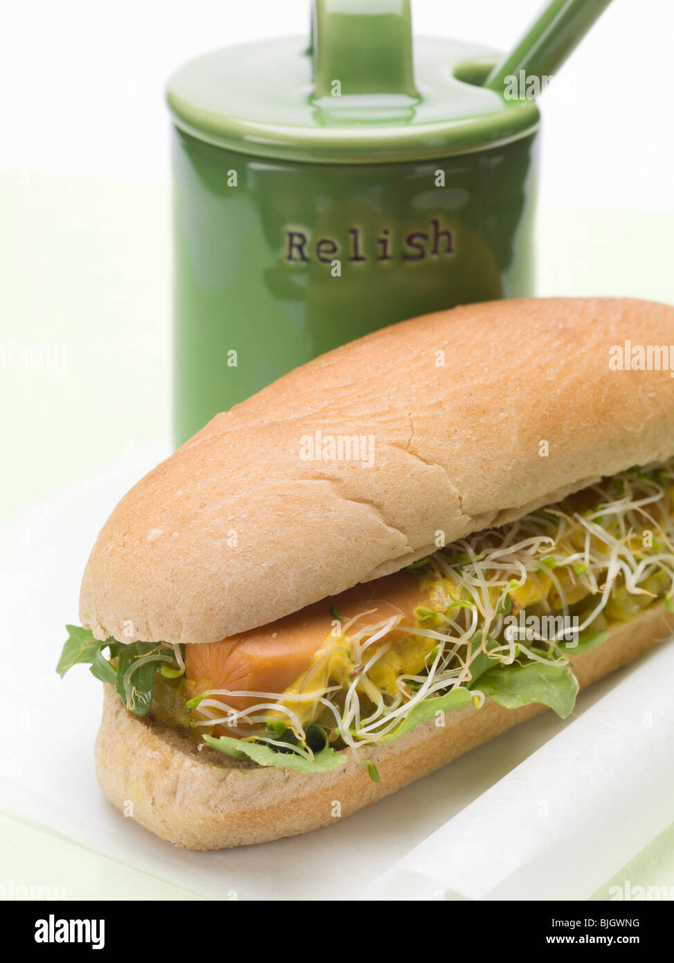 A hot dog with sprouts beside a relish pot - Stock Photo