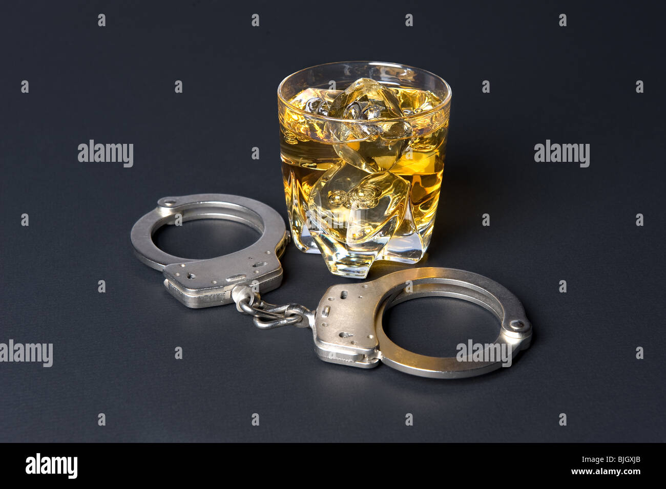 A pair of handcuffs next to a glass of whiskey infers that drinking and