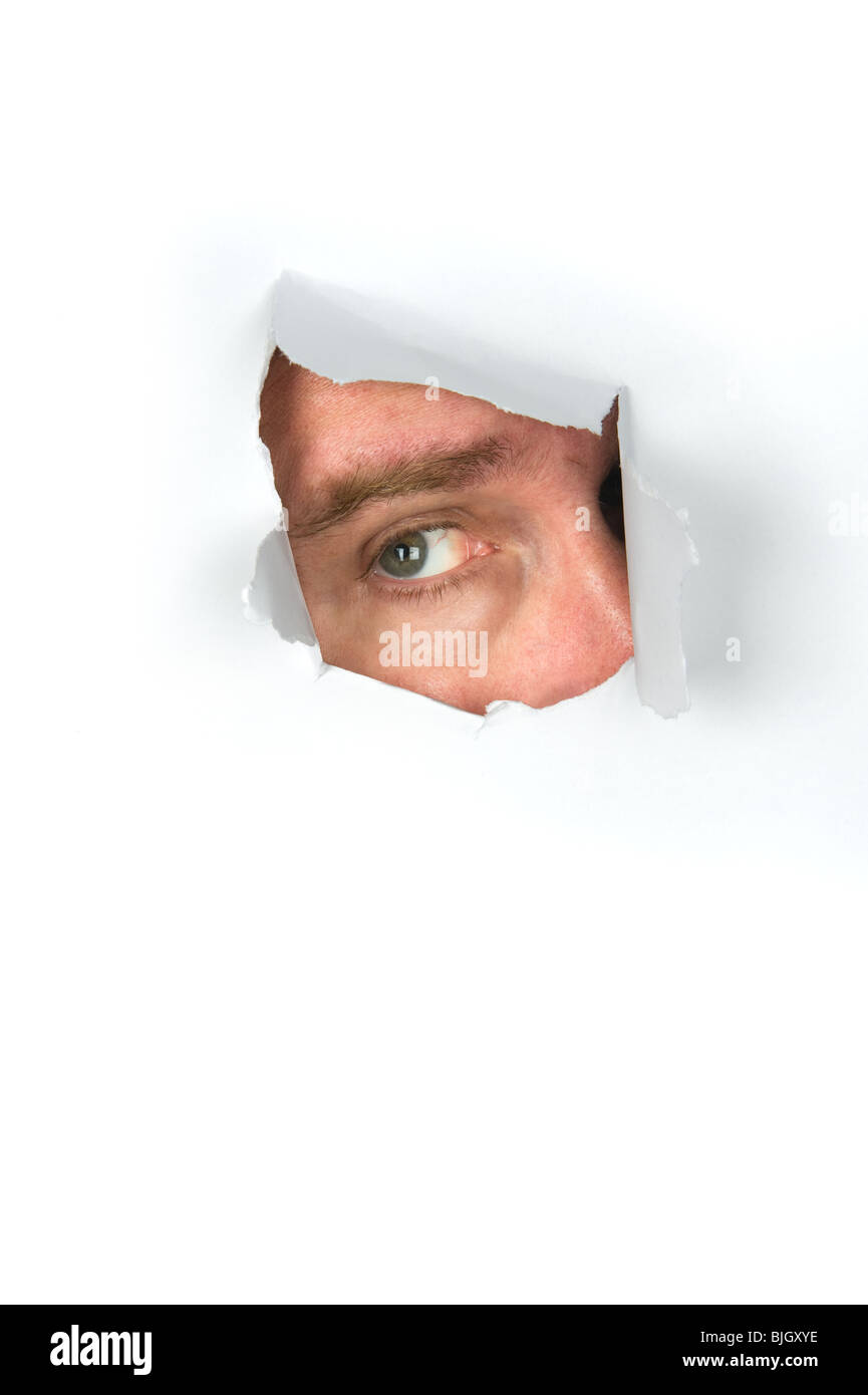 A man peers through a torn paper hole. Stock Photo