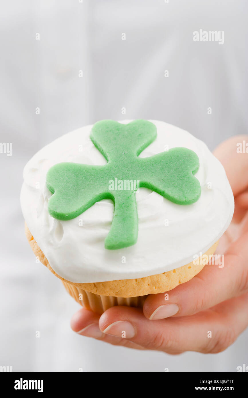 Hand holding cupcake with marzipan clover leaf - Stock Photo
