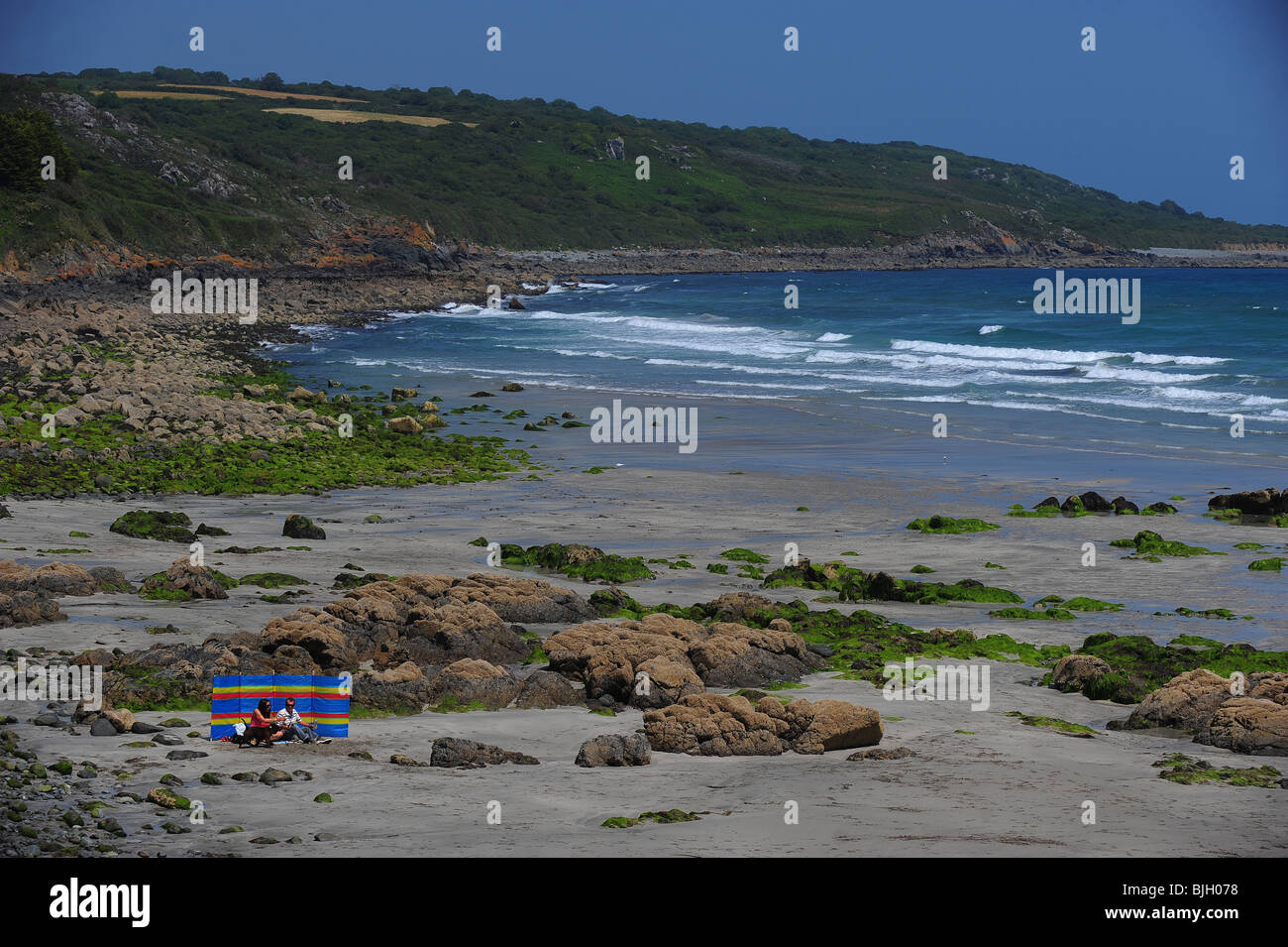 Two people sunbathing with a windbreak at an empty Coverack Beach, Cornwall uk Stock Photo
