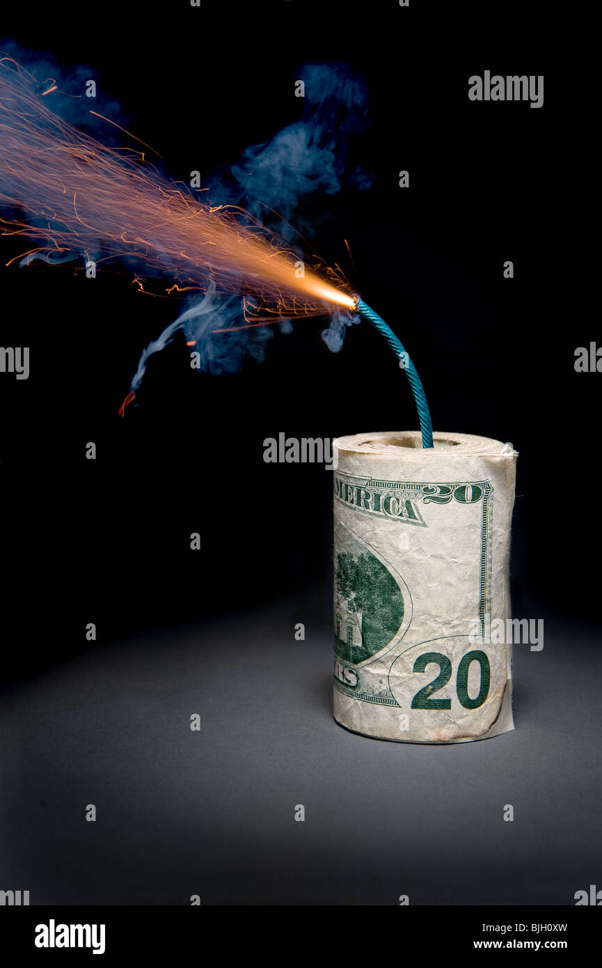 A roll of cash made into a dynamite stick has a lighted fuse throwing smoke and sparks before it explodes. Stock Photo