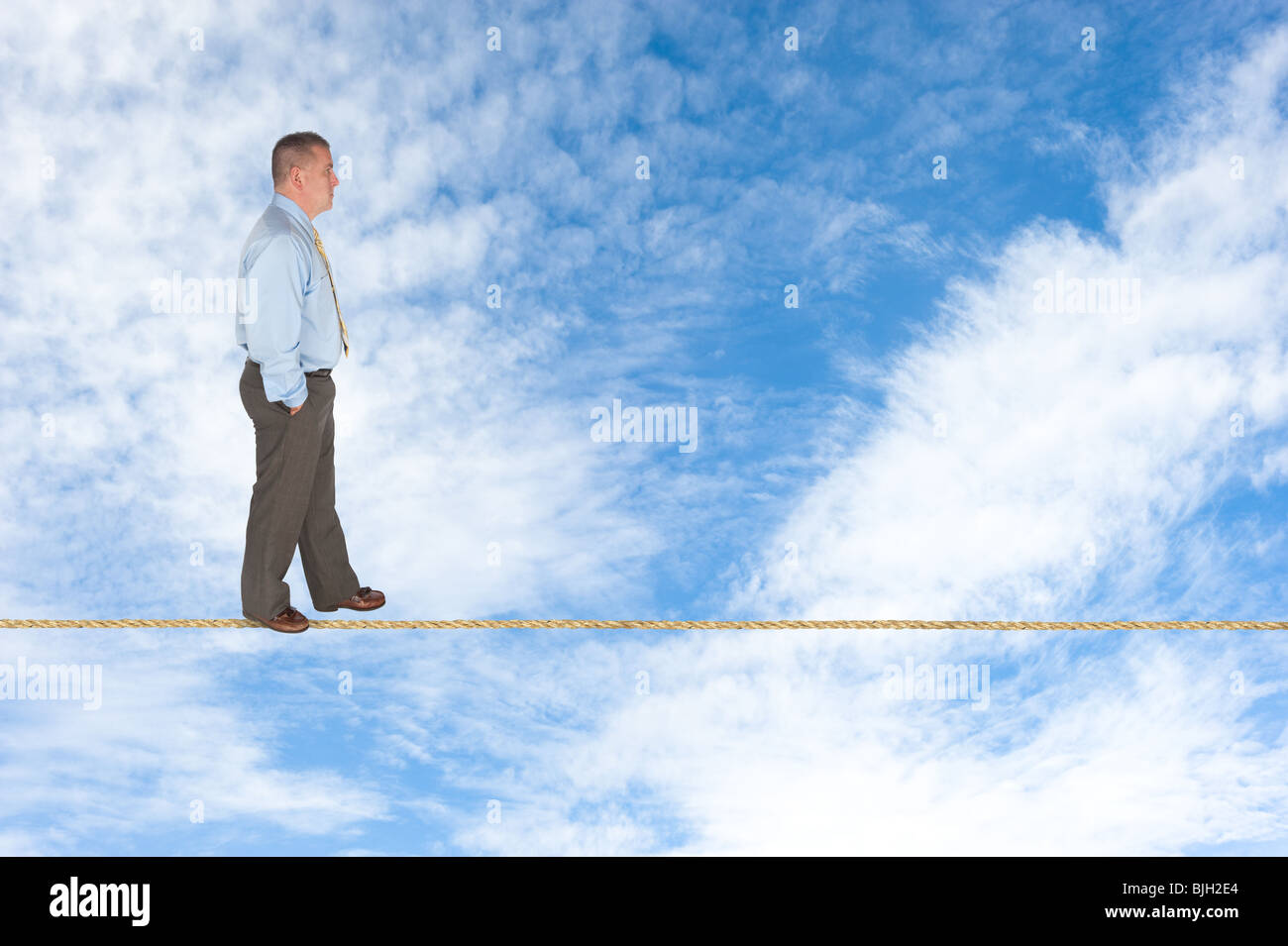 A businessman walks across a tightrope contemplating success, risk, vision and the way forward. Stock Photo