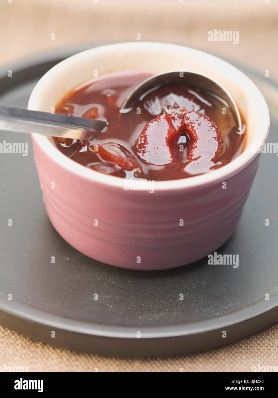Spiced plum sauce in dish with ladle - Stock Photo