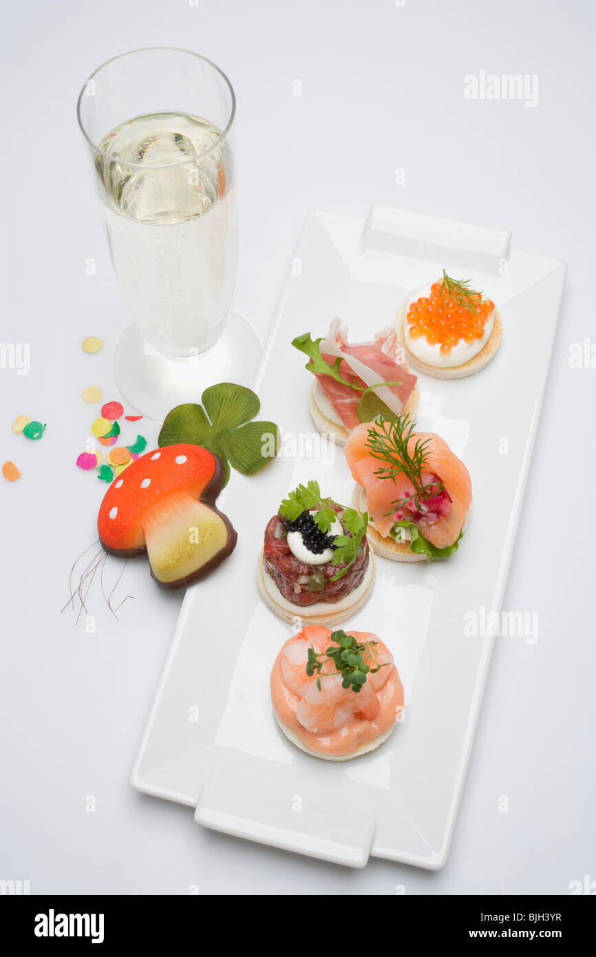 Canapés, glass of sparkling wine, good luck charms for New Year - Stock Photo