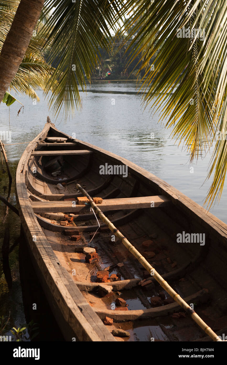 India, Kerala, Alleppey, Alappuzha, backwaters small wooden boat moored on riverbank below coconut palm tree Stock Photo