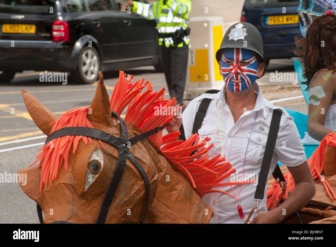 Man with hobby horse, Union Jack painted face and police helmet in