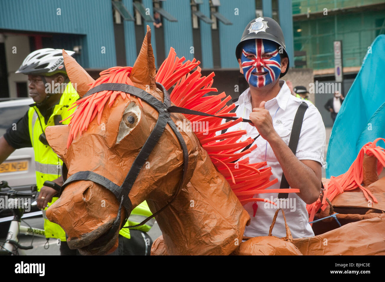 Man with hobby horse, Union Jack painted face and police helmet in