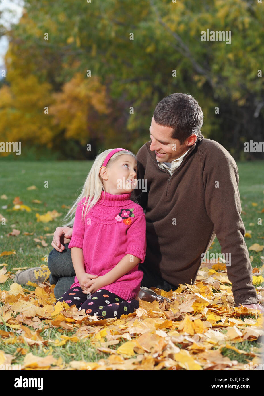 attractive father and daughter sitting in autumn leaves outdoors Stock Photo